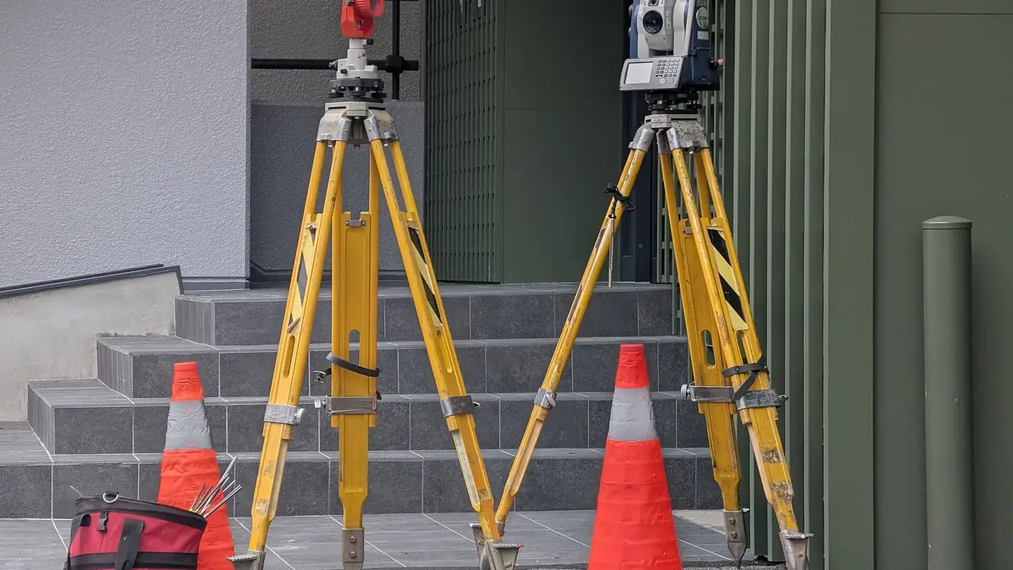 Station totale et prisme sur trépieds, balisés par des cônes devant un bâtiment