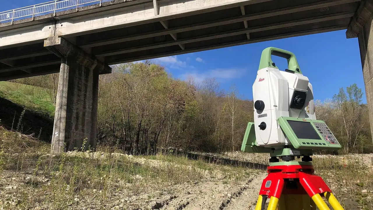Station totale sur trépied installée sous un pont pour un levé topographique